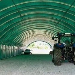 Vue intérieure d'une serre tunnel verte abritant un tracteur et une voiture, montrant l'espace disponible à l'intérieur.