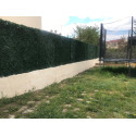 Vue latérale d'une haie artificielle 243 brins posée dans un jardin familial avec trampoline en arrière-plan