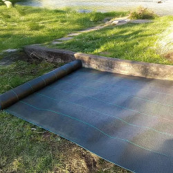 Rouleau de toile de paillage noire 130g/m² en cours de pose au sol pour limiter la repousse des mauvaises herbes dans un jardin