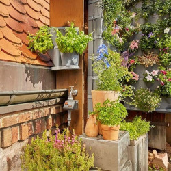 Installation complète du kit NatureUp! Gardena sur balcon, avec jardinières verticales, plantes aromatiques et fleurs colorées.