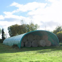 Abri tunnel agricole Deschamps de 6 m de large avec bottes de foin stockées à l’intérieur, bâche verte tendue.