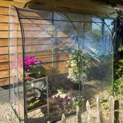 Serre de jardin adossée 2 m² installée contre un mur en bois, avec fleurs et plantes à l'intérieur