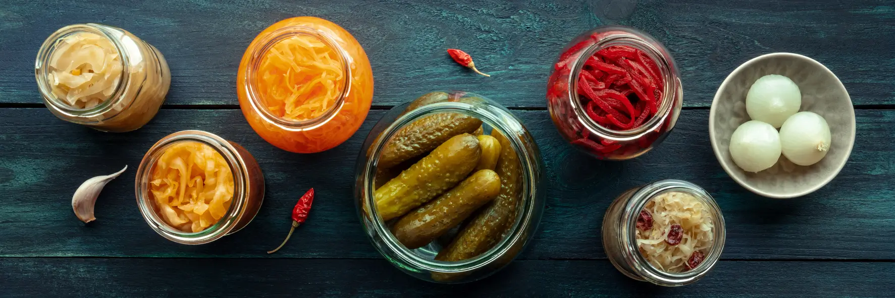 Bocaux et pickles de légumes d'été : cornichons, oignons,... déposé sur une table en bois