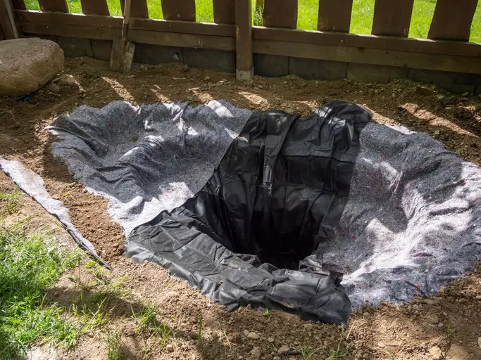 Un trou creusé dans le sol avec une toile de protection en place, prêt pour la construction d'un étang de jardin.